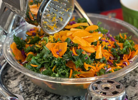 metal bowl that contains shredded yellow orange persimmons and dark green kale